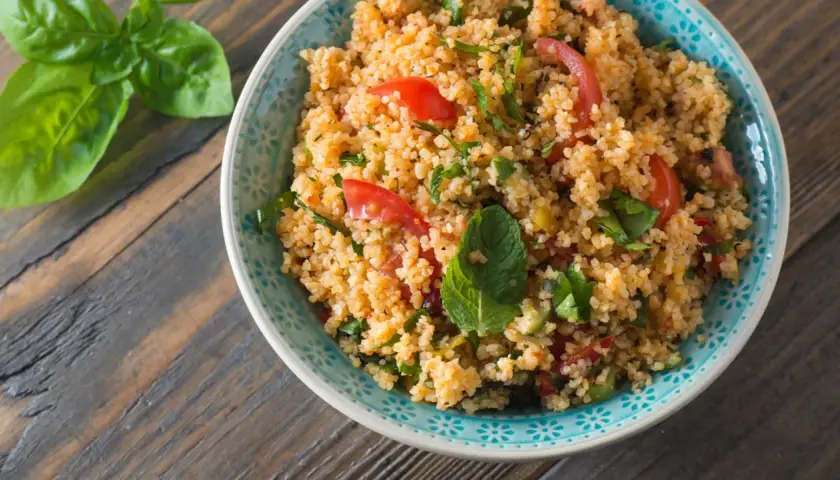 Una ciotola di insalata di cous cous con pomodorini e erbe fresche, pronta per essere gustata.