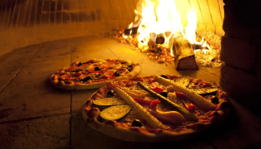 Zwei Pizzen im Holzofen, die Hitze des Feuers sorgt für die perfekte pizza ofen temperatur.