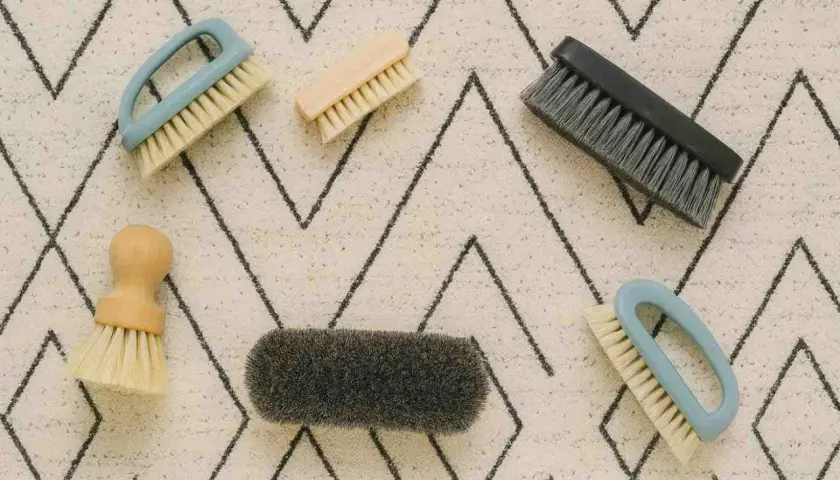 Cinco cepillos de diferentes tamaños y colores sobre una alfombra con patrón de zigzag. Herramientas perfectas para saber como limpiar alfombras a mano.