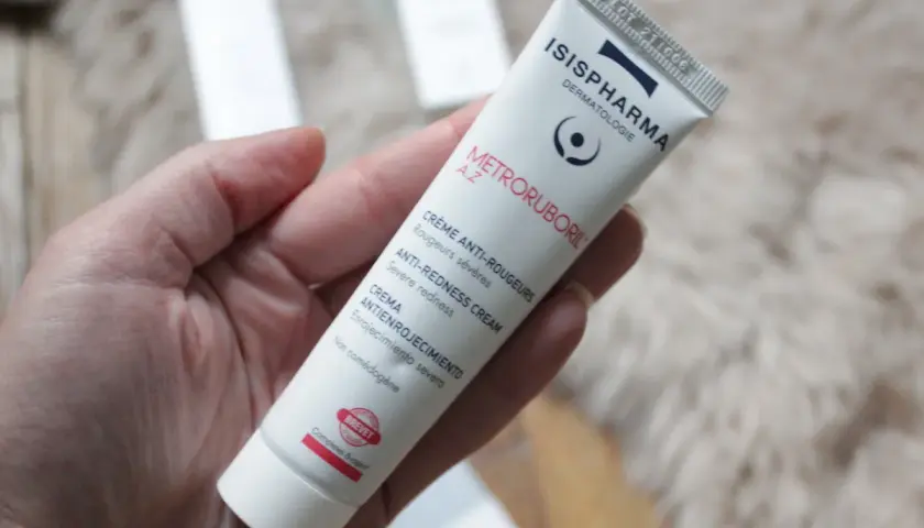 Une main tient un tube de crème anti-rougeurs de la marque Isispharma, contenant de l'acide azélaïque pour apaiser les rougeurs sévères.