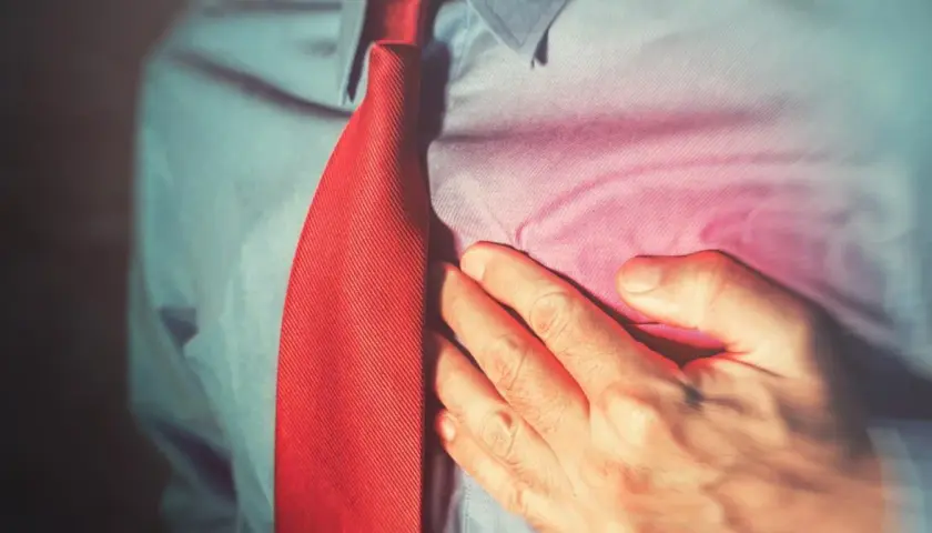 Mężczyzna w koszuli i czerwonym krawacie trzyma się za serce. Może to być sygnał, że potrzebuje leku, np. Betaloc.