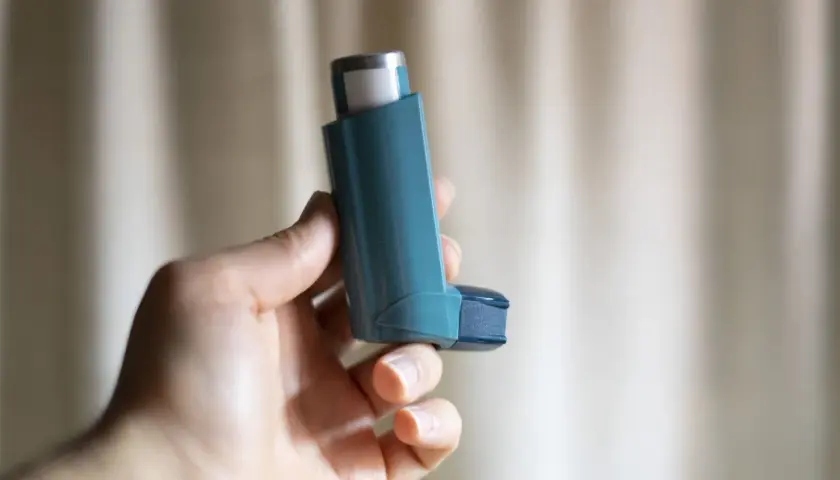 Dłoń trzyma niebieski inhalator z salbutamolem, gotowy do ulgi w astmie.