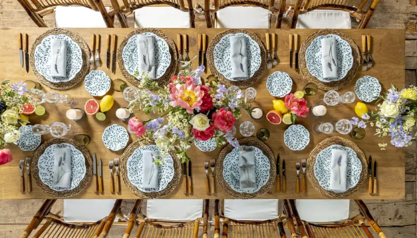 Table dressée pour un repas mariage champêtre, avec fleurs, fruits et vaisselle décorée de feuilles vertes.