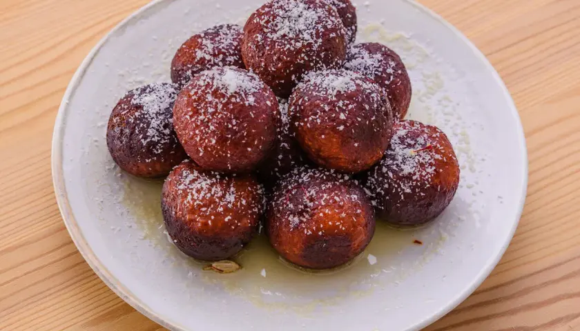 En hög med söta, mörka gulab jamun, pudrade med kokosflingor och serverade i en ljus sirap.
