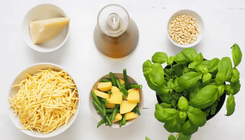 Ingredienti per un pesto senza pinoli: basilico fresco, formaggio grattugiato, patate, fagiolini, olio e aglio.