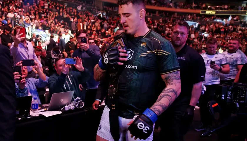 Mistrz UFC z pasem na ramieniu, otoczony tłumem fanów robiących zdjęcia.
