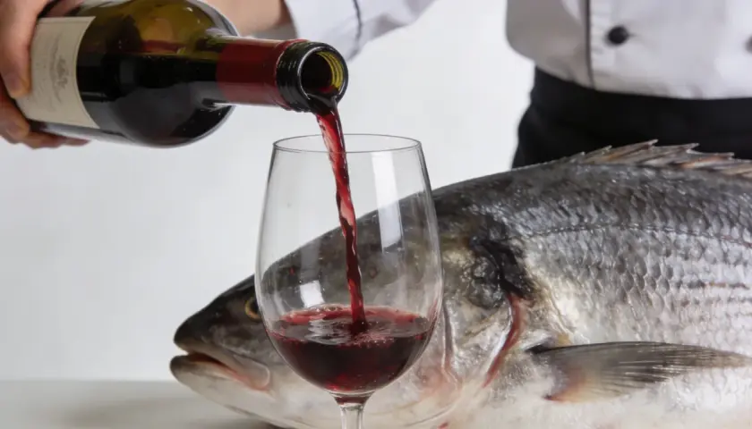 Un chef verse du vin rouge dans un verre, à côté d'un poisson entier. Une question se pose : quel vin rouge avec du poisson ?