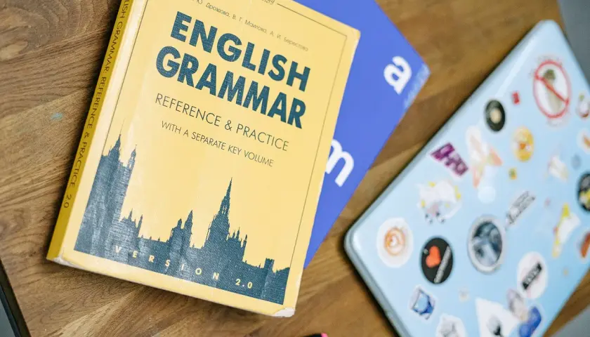 Książka "English Grammar: Reference & Practice" i niebieski notatnik leżą na drewnianym blacie. Idealne do nauki zadań gramatycznych angielskiego.