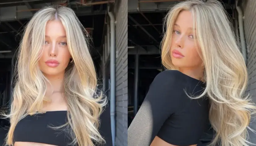 Blond włosy z subtelnym scandi hairline, falowane i pełne objętości, opadają na ramiona.