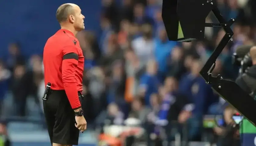 Sędzia w czerwonej koszulce czeka na decyzję VAR, która może skutkować żółtą kartką.