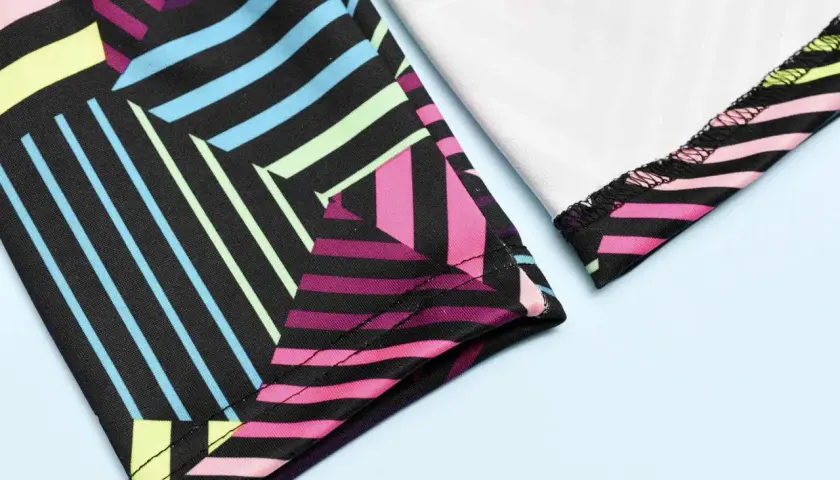 Close-up of colorful geometric leggings. The fabric is black with vibrant stripes of pink, blue, yellow, and green. The stitching shows how you can sew leggings.