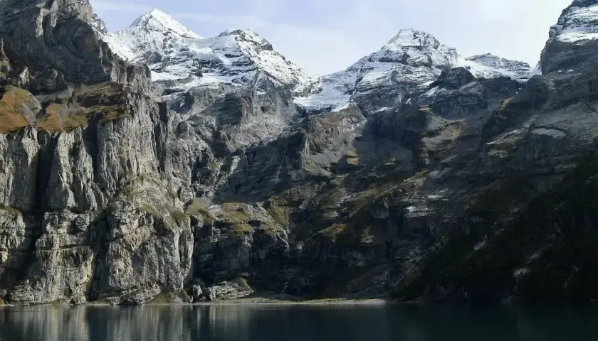 Majestatyczny łańcuch górski z ośnieżonymi szczytami, przypominający Tatry, odbija się w spokojnej tafli jeziora.