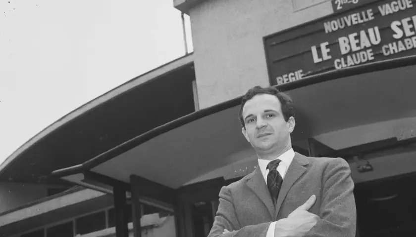 Jean Pierre Léaud w garniturze, z rękami skrzyżowanymi na piersi, przed budynkiem z napisem "Le Beau Serge".