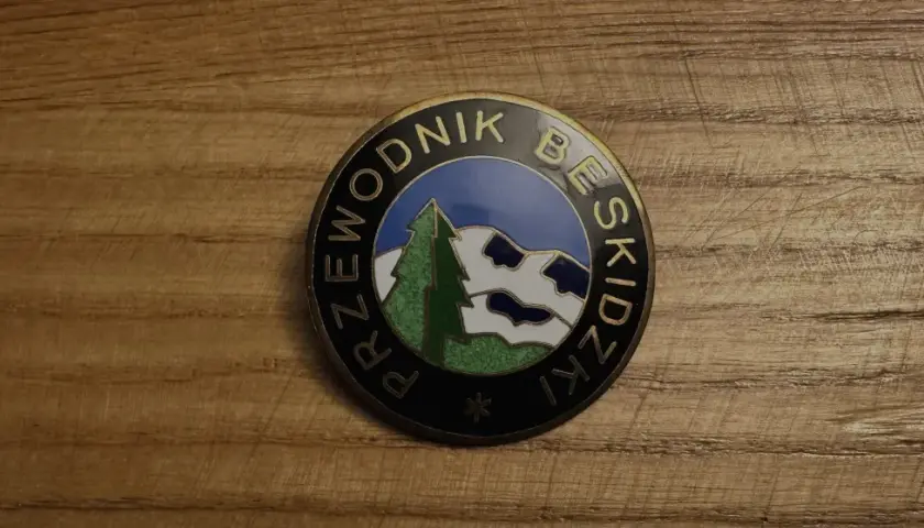 Odznaka z napisem "Przewodnik Beskidzki" i malowniczym krajobrazem górskim.