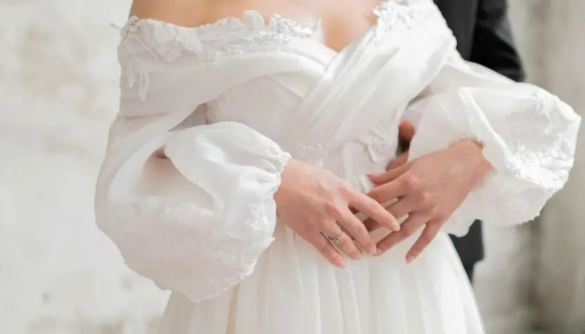 Delikatne makijaże weselne podkreślają urodę panny młodej w zwiewnej sukni. Dłonie z pierścionkiem spoczywają na materiale.