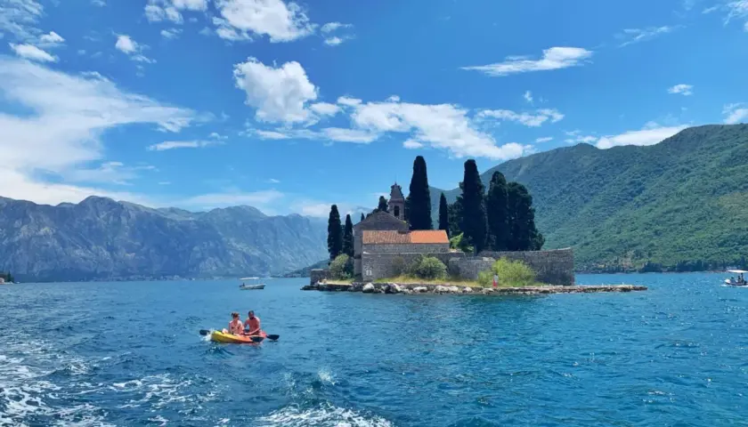 Kayaking in Montenegro's Bay of Kotor, a perfect spot for any trip planner. Mountains and a church on an island create a stunning backdrop.