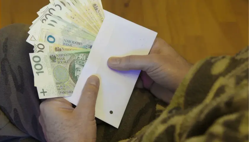 Dłonie trzymające kopertę z polskimi banknotami.
