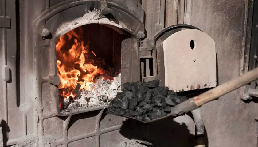 Fachowiec od pieca zasypuje węglem palenisko, gdzie szaleje ogień.