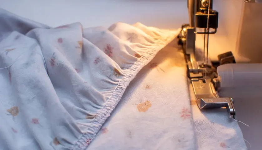 A serger creates a gathered edge on a floral-patterned fabric, preparing it for a sewing project.