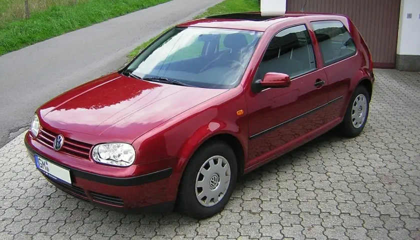 Czerwony Volkswagen Golf IV zaparkowany na podjeździe z kostki brukowej, obok garażu.