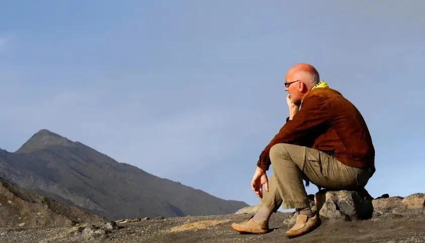 A man in hiking gear sits on a rock, contemplating the vast, barren landscape. This is the essence of zero day hiking, a moment of quiet reflection before the real adventure begins.