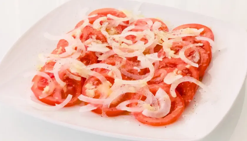 Una refrescante ensalada de tomate y cebolla, aderezada con sal y pimienta, lista para disfrutar.