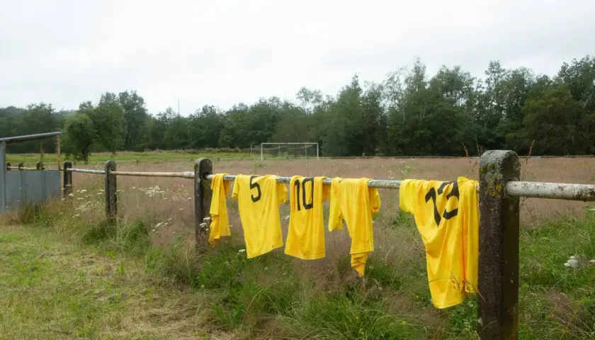 Maillots de foot jaunes floqués, numéros 5, 10, 12, sèchent sur une barre rouillée. Une astuce pour savoir comment laver un maillot de foot floqué.