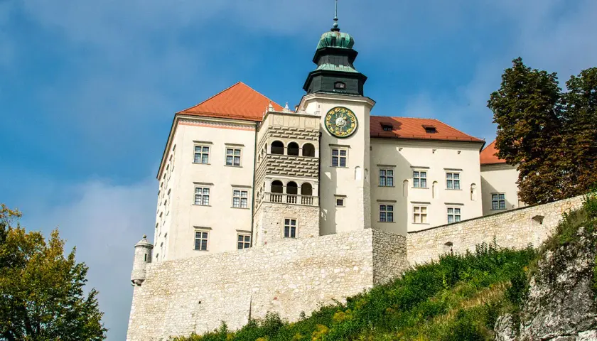 Zamek na Pieskowej Skale, biały z czerwonym dachem, z wieżą zegarową, na tle błękitnego nieba.
