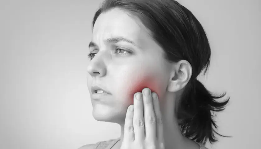 Mujer con dolor en la mejilla, indicando un posible flemón por muela del juicio.