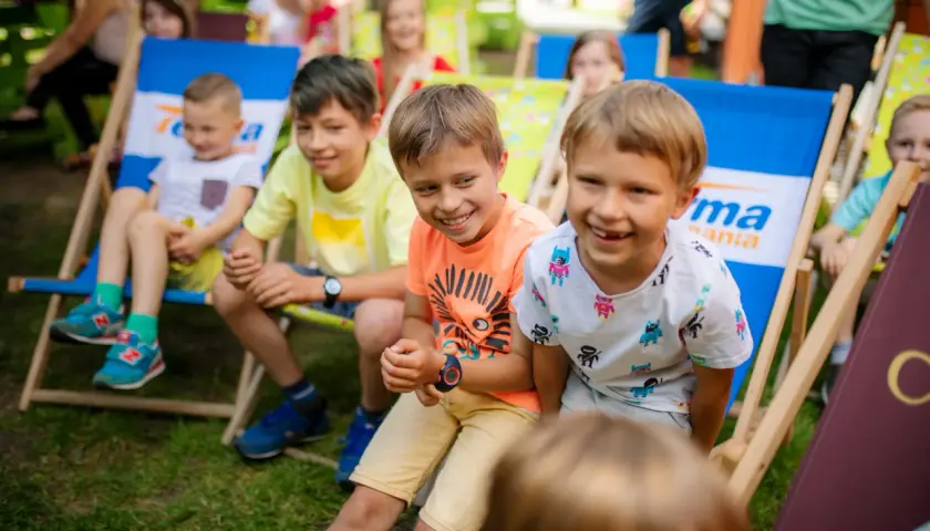 Uśmiechnięte dzieci siedzą na leżakach w parku. To idealne miejsce na letnie zabawy, jak w najlepszych parkach dla dzieci.