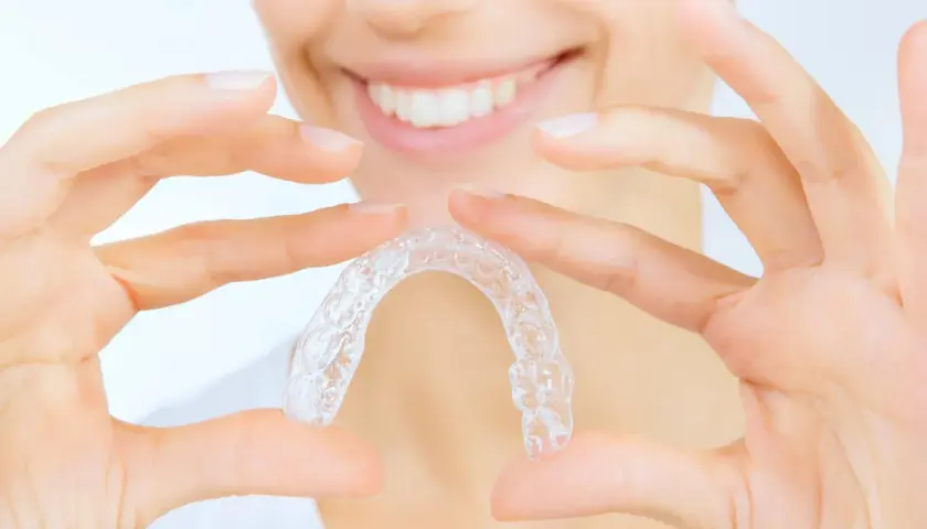 Manos sostienen un alineador transparente, mostrando cómo quitar Invisalign para una sonrisa perfecta.
