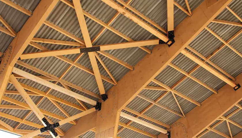 Structure complexe de poutres en bois de type **lvl bois**, soutenant un toit ondulé.