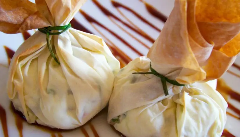 Dos saquitos de pasta filo rellenos, atados con hilo verde, reposan sobre un plato con un glaseado oscuro.