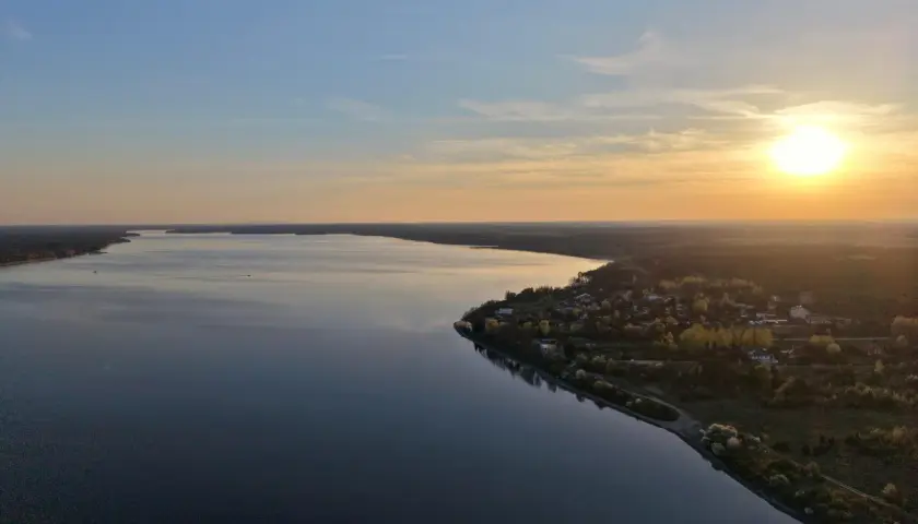 Zachód słońca nad Zalewem Sulejowskim. Woda odbija niebo, a na brzegu widać domki i drzewa. To idealne miejsce na relaks i podziwianie pięknych widoków, prawdziwe zalew sulejowski atrakcje.