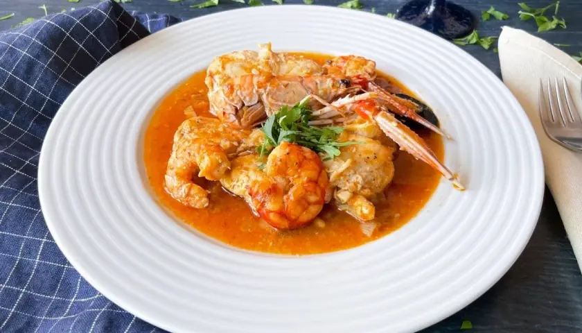 Rape en salsa con gambas y cigalas, servido en plato blanco con perejil fresco.
