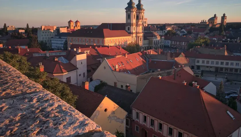 Widok na Eger z zamku o zachodzie słońca. Czerwone dachy, barokowa bazylika i wieże kościelne w złotym blasku.