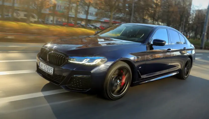 Ciemnoniebieskie BMW 540d sunie po drodze, odbijając jesienne słońce.