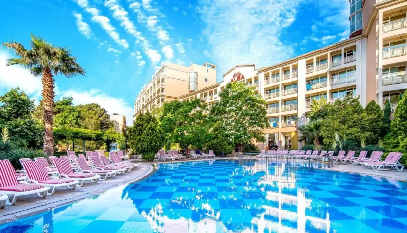 Basen z leżakami i palmą przy hotelu Alba w Bułgarii. Słoneczny dzień, błękitne niebo z chmurami.