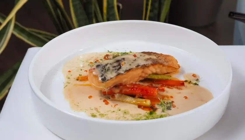 Un filet de poisson poêlé, baignant dans une onctueuse sauce champagne, accompagné de légumes croquants et de quelques perles orangées.