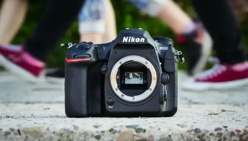 Nikon D500 na kamieniu, z rozmazanymi nogami w tle. Chcesz wiedzieć, jak sprawdzić przebieg aparatu Nikon?