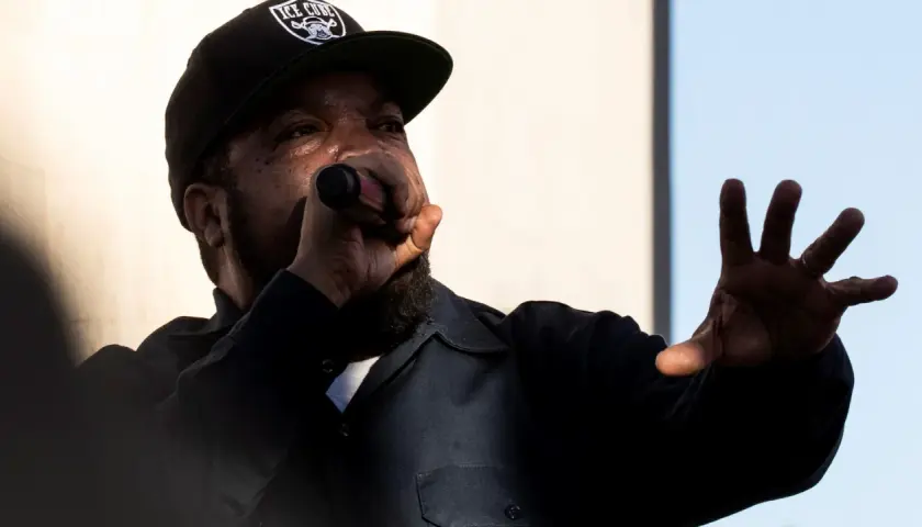 Raper Ice Cube w czapce z daszkiem "ICE CUBE" śpiewa do mikrofonu, gestykulując ręką. Jego styl to klasyczny diss.