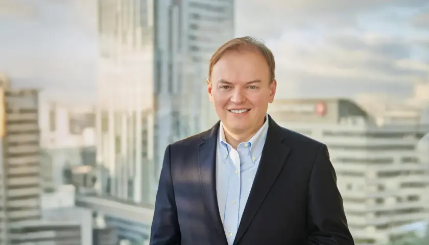 Uśmiechnięty mężczyzna w garniturze, cfo, stoi na tle nowoczesnych wieżowców.