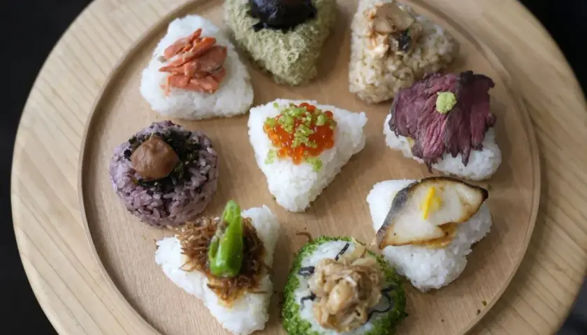 A colorful assortment of Japanese triangle food, including onigiri with salmon, beef, fish, and ikura, arranged on a wooden platter.