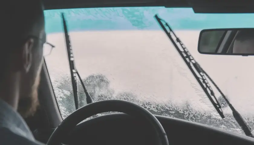 Conductor con gafas y barba, mira a través del parabrisas mojado. ¿Qué hacer si llueve y no anda el limpiaparabrisas?