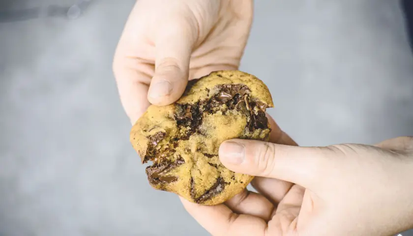 Hände halten einen zerkrümelten Schokoladenkeks, der nach einem einfachen Cookies Rezept gemacht wurde.