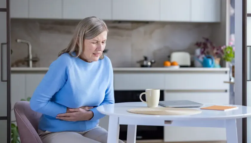 Donna anziana con le mani sull'addome, soffre di problemi di digestione. Le cause possono essere molteplici.