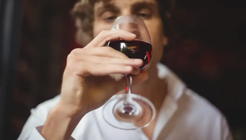 Un homme déguste un verre de vin rouge, réfléchissant aux termes pour qualifier le vin.