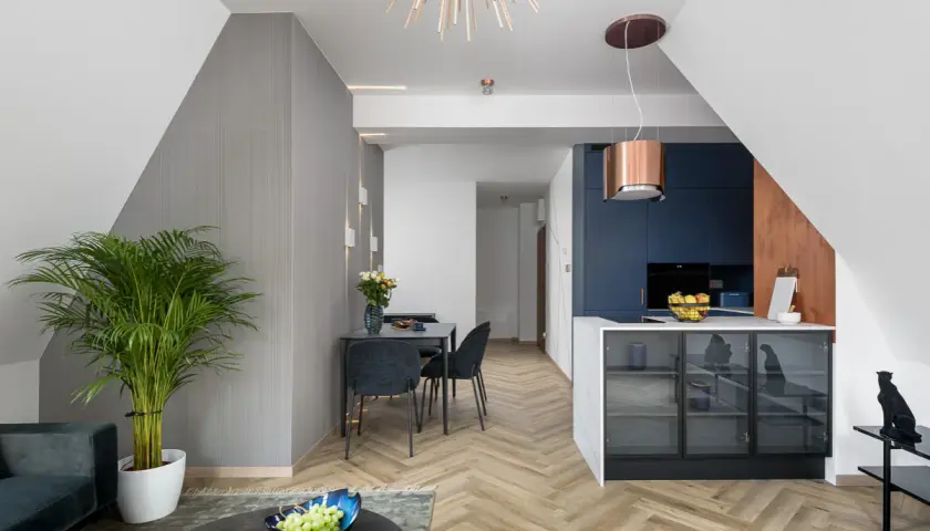 Nowoczesna kuchnia z granatowymi frontami i miedzianym okapem. W salonie elegancka jadalnia i duża palma. Domowe rewolucje w stylowym wydaniu.
