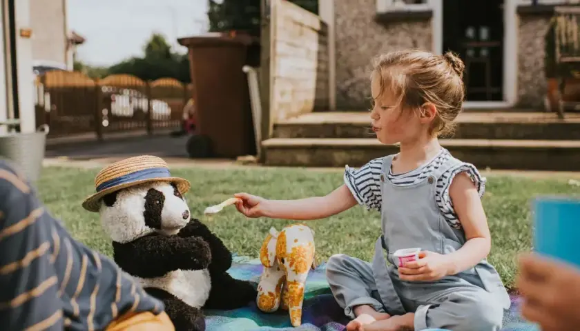 Dziewczynka karmi pluszową pandę na pikniku. Wspaniałe zabawy dla 5-6 latków w domu i ogrodzie.