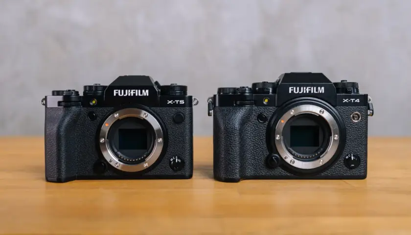 Dwa aparaty Fujifilm: X-T5 i X-T4, stojące obok siebie na drewnianym stole.